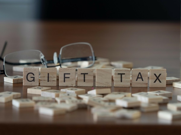 "Gift Tax" represented by wooden letter tiles on a wooden table with glasses and a book.