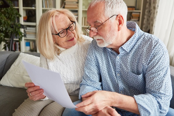 An elderly couple from Boca Raton, FL, sitting together on a sofa, looking over a legal document with a focused and supportive expression, representing the process of estate planning or establishing a power of attorney.